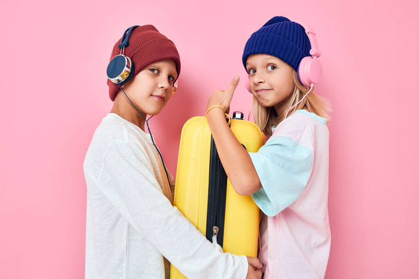 Portret dziewczynki i chłopca żółta walizka ze słuchawkami w odizolowanym tle - Zdjęcie, obraz