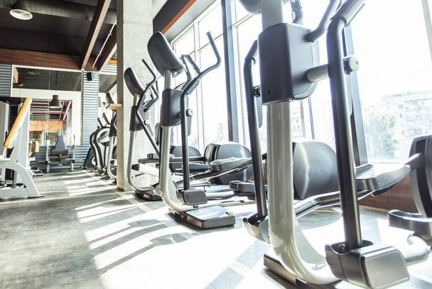 Interior moderno del gimnasio con equipos de fitness y máquinas de ejercicio. Pabellón deportivo con grandes ventanales - Foto, Imagen