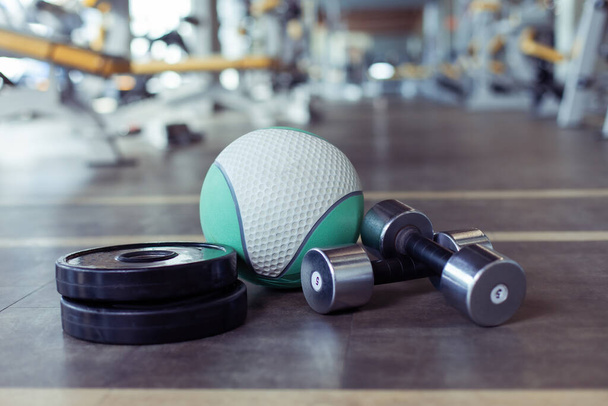 Mancuernas de metal, discos de barra y bola de medicina en el piso del gimnasio. Fitness, musculación y entrenamiento funcional - Foto, imagen