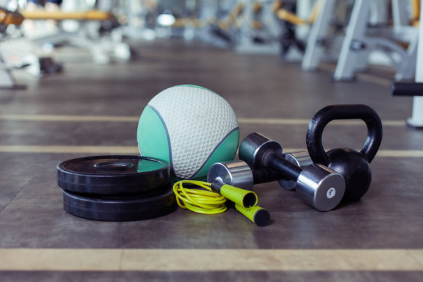 Металеві гантелі, диски барбелла, чайник, пропускаюча мотузка та медичний м'яч на підлозі спортзалу. Фітнес, бодібілдінг та функціональне тренувальне обладнання
 - Фото, зображення