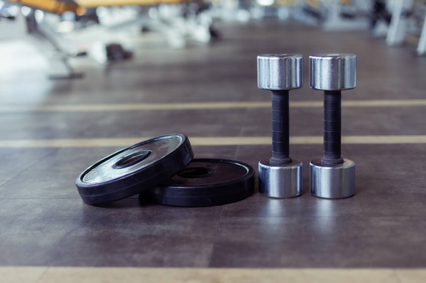 Manubri in metallo e dischi di bilanciere sul pavimento della palestra. Attrezzature per fitness, bodybuilding e allenamento funzionale - Foto, immagini