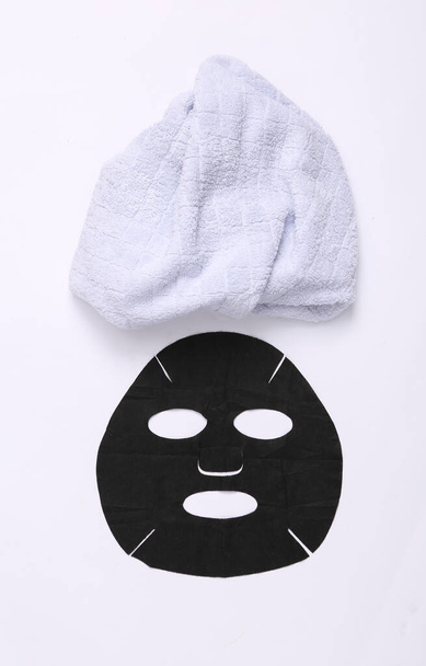 Μαύρη μάσκα καθαρισμού και πετσέτα σε λευκό φόντο. Διαδικασίες Spa, έννοια της προσωπικής φροντίδας - Φωτογραφία, εικόνα