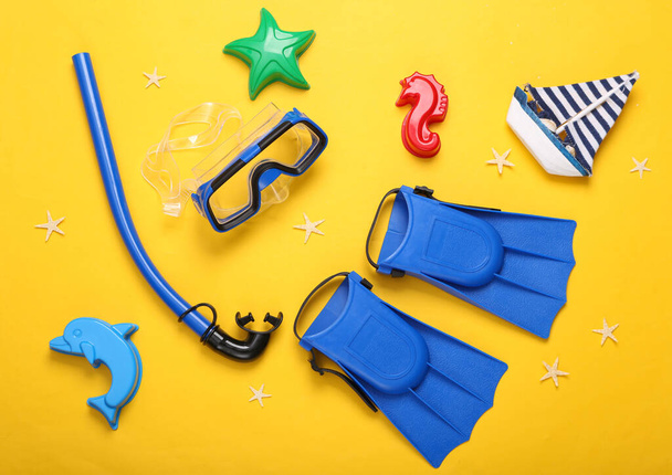 Children's beach accessories. Diving set and sand toys on a yellow background. Top view - Photo, Image