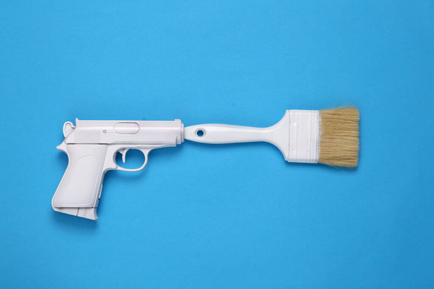 Weiße Pistole mit Pinsel auf blauem Hintergrund. Minimales, kreatives Layout, Draufsicht - Foto, Bild