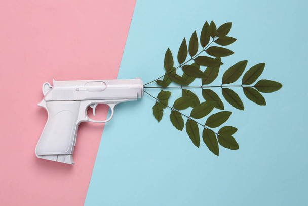 Weiße Pistole mit grünen Blättern auf blau-rosa Hintergrund. Minimales, kreatives Layout, sagt nein zum Krieg - Foto, Bild