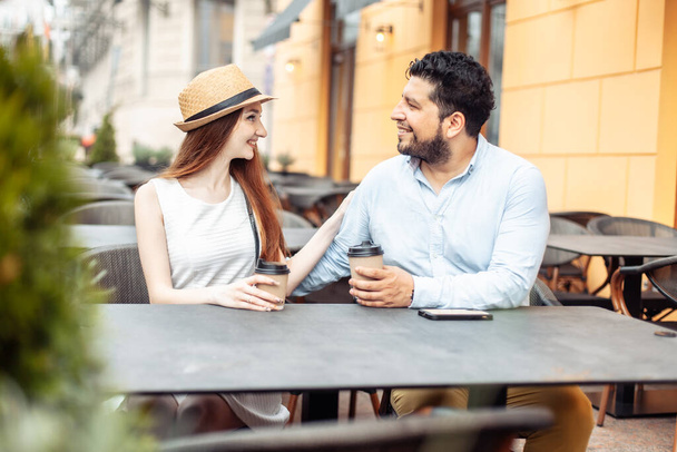 International couple in love drinking coffee while sitting at table in outdoor cafe - Photo, Image