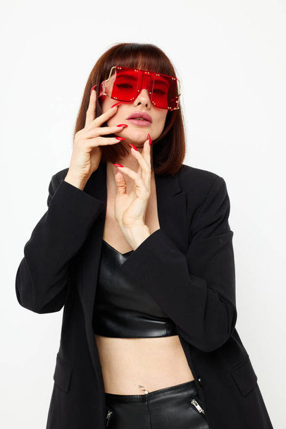portrait of a woman in a black jacket red nail polish fashion glasses light background - Foto, Imagem
