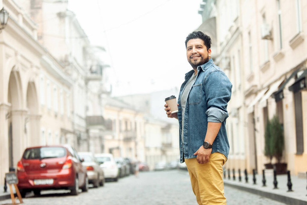 Handsome smiling hispanic guy drinking coffee in the city - Photo, image
