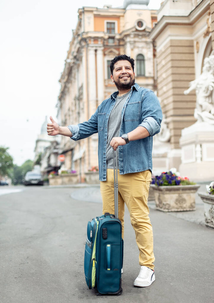 Hispanic man tourist with travel luggage catch ride in the city. Travel concept. Hitchhiking - Фото, изображение