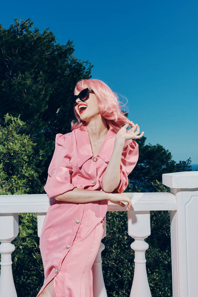 mujer hermosa vestido rosa estilo moderno se encuentra cerca de la barandilla inalterada - Foto, Imagen