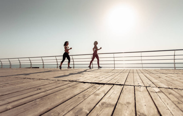 İki atletik bayan arkadaş sabahın erken saatlerinde sette koşuyorlar. - Fotoğraf, Görsel