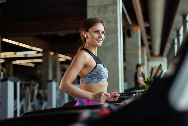 Junge, fitte Frau joggt auf einem Laufband in einem modernen Fitnessstudio. Ausdauertraining - Foto, Bild
