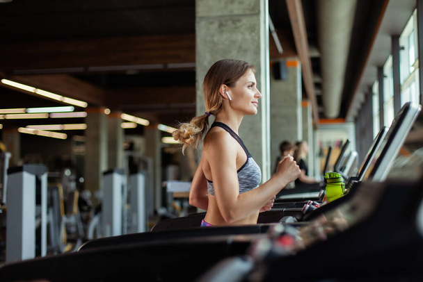 Mladá fit žena běhá na běžeckém pásu v moderní tělocvičně. Cvičení na kardiologii - Fotografie, Obrázek