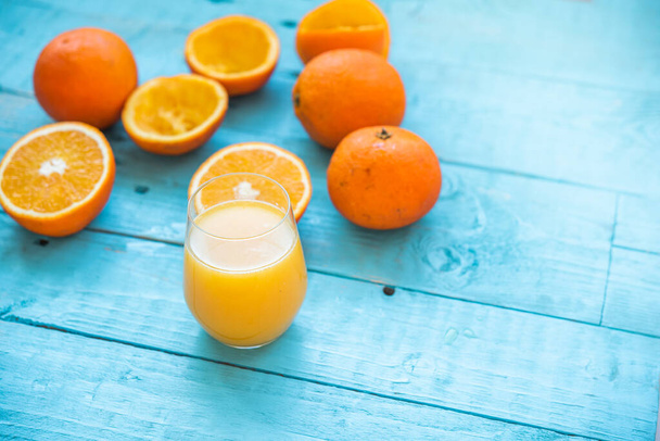 いくつかの有機オレンジ、いくつかの全体の自然なジュースのガラス、いくつかの圧迫は、食事のために、青い木製のテーブルの上に。健康的な朝食 - 写真・画像