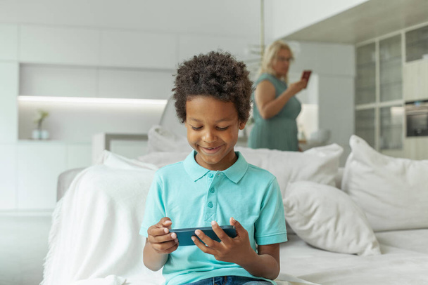 Happy child boy with smartphone on blurred background from mother with phone at home - Photo, Image