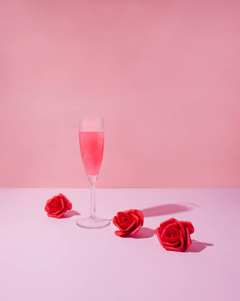 Romantic party concept. Pink drink in champagne glass and red roses against pink background. St Valentine's day creative idea - Fotó, kép