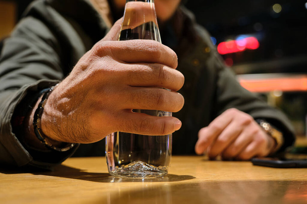 Szklanka wody, butelka wody wisząca na męskiej ręce. Selektywne zdjęcie ostrości wewnątrz kawiarni - Zdjęcie, obraz