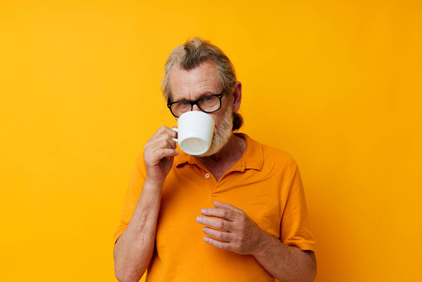 Senior grey-haired man in a yellow t-shirt white mug isolated background - Valokuva, kuva