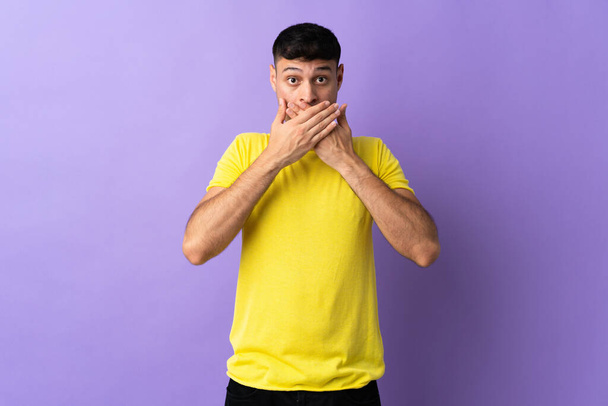 Mladý kolumbijský muž izolované na fialovém pozadí zakrývající ústa s rukama - Fotografie, Obrázek