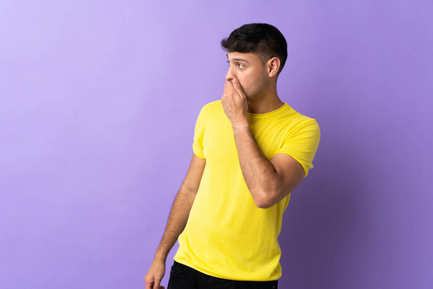Young Colombian man isolated on purple background doing surprise gesture while looking to the side - Photo, Image