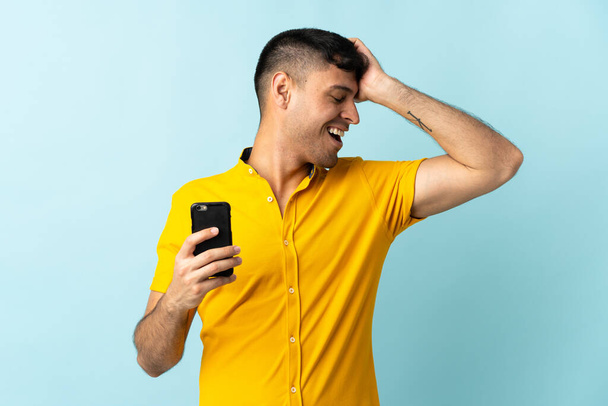 Mladý kolumbijský muž používající mobilní telefon izolované om modré pozadí si něco uvědomil a zamýšlí řešení - Fotografie, Obrázek