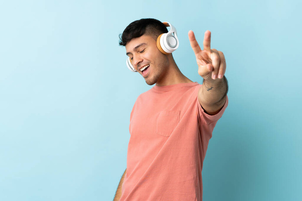 Joven colombiano aislado sobre fondo azul escuchando música y cantando - Foto, Imagen