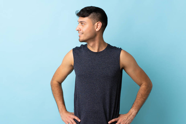 Young Colombian man isolated on blue background posing with arms at hip and looking side - Fotografie, Obrázek