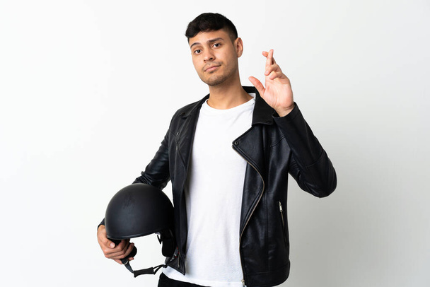 Uomo con un casco moto isolato su sfondo bianco con le dita incrociate e augurando il meglio - Foto, immagini