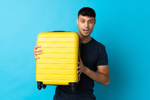 若いコロンビア人男性隔離上の青の背景で休暇で旅行スーツケースと驚き - 写真・画像