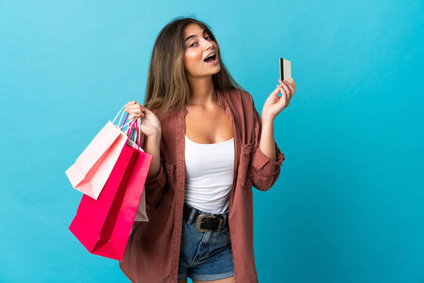 Young caucasian woman isolated on blue background holding shopping bags and a credit card - Zdjęcie, obraz