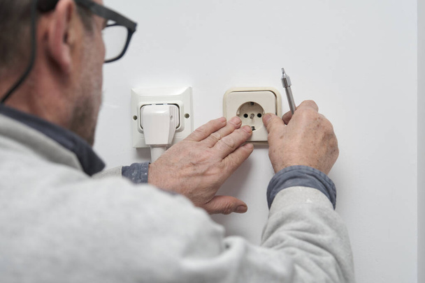 Senior-Elektriker installiert einen Stecker in einem neuen Haus. - Foto, Bild