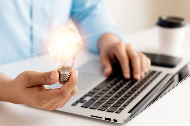 Successful Innovation through ideas and inspiration ideas. Human hand holding light bulb to illuminate, idea of creativity and inspiration concept of sustainable business development. - Фото, изображение