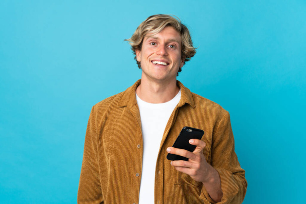 携帯電話を使用して隔離された青い背景の上に英語の男 - 写真・画像