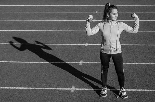 healthy child girl training fitness with dumbbells on stadium running track, weigh lifting - Valokuva, kuva