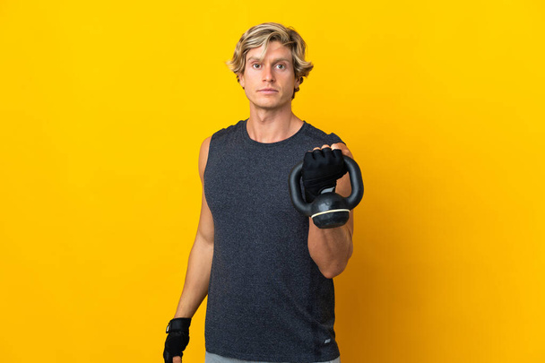 English man over isolated yellow background making weightlifting with kettlebell - Fotoğraf, Görsel