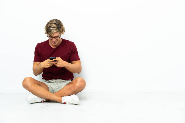 Jeune Anglais assis sur le sol envoyant un message avec le mobile - Photo, image
