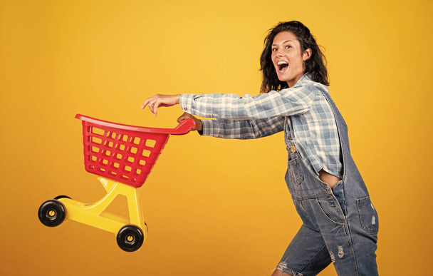prepare for holidays. happy beautiful lady carry shopping trolley. time to shop. female shopaholic in action. cheerful woman making purchase. girl with stylish brunette hair in store - Foto, Imagem
