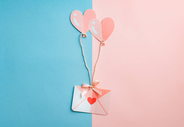 Gefeliciteerd met Valentijnsdag. Een envelop met een hart dat op twee hartvormige ballonnen vliegt is roze. - Foto, afbeelding