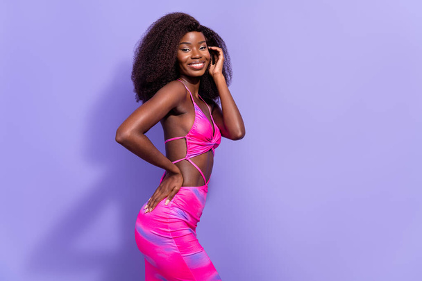 Foto van charmante dromerige afro meisje dragen pint sexy outfit hand wang jukbeen lege ruimte glimlachen geïsoleerde paarse kleur achtergrond - Foto, afbeelding