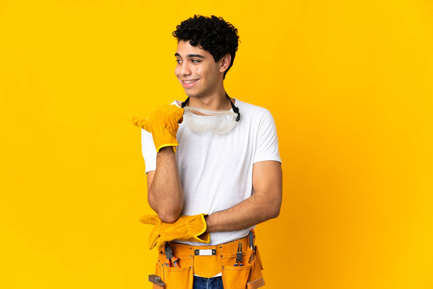Venezuelan electrician man isolated on yellow background pointing to the side to present a product - Photo, Image