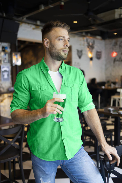 Un bel homme en vert tenant sa bière dans un pub pour la Saint Patrick - Photo, image