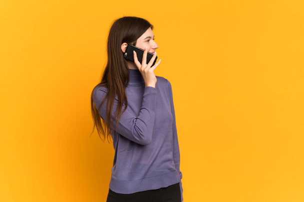 Giovane ragazza ucraina isolata su sfondo giallo mantenendo una conversazione con il telefono cellulare con qualcuno - Foto, immagini