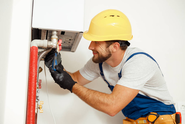 Vue latérale du bricoleur, technicien utilisant un tournevis lors de la fixation de la chaudière ou du chauffe-eau, travaillant sur le système de chauffage dans l'appartement - Photo, image