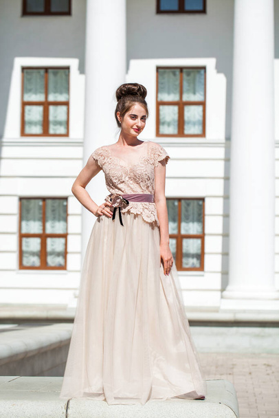 Young beautiful brunette in a luxurious beige dress posing on the street - Fotografie, Obrázek
