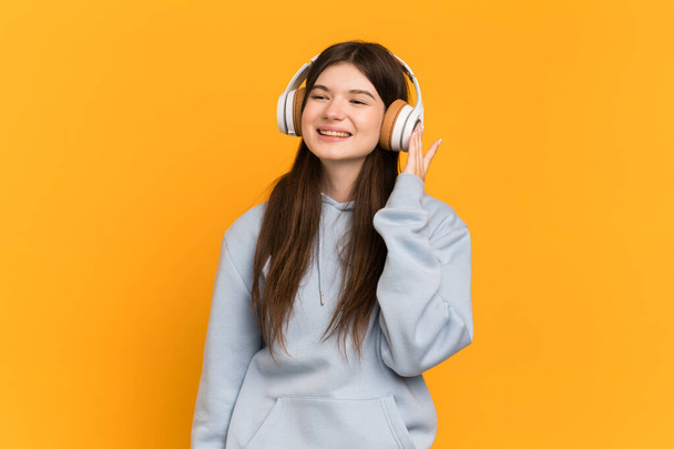 Young Ukrainian girl isolated on yellow background listening music - Zdjęcie, obraz