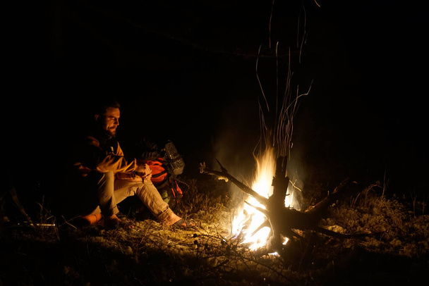 Sakhalin, Russia - October 17, 2020: Hiker warming himself by the fire in the taiga - 写真・画像