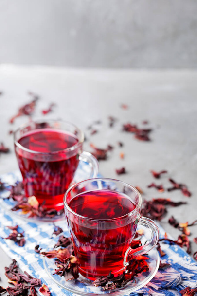Hibiscus tea and dry hibiscus petals on gray background. Two glass cups of red hibiscus tea on blue napkin. Top view. Copy space - Foto, imagen