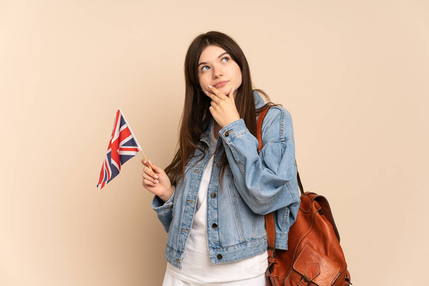 Junge Ukrainerin mit einer britischen Flagge auf beigem Hintergrund, die lächelnd nach oben blickt - Foto, Bild