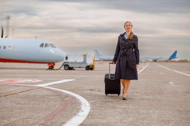 Havaalanında yürüyen seyahat valizli gülümseyen kadın. - Fotoğraf, Görsel