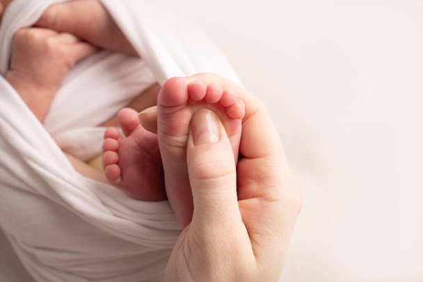 Äiti hieroo vauvajalkaansa. Lähemmäs vauvan jalat äidin käsissä. Litteiden jalkojen ehkäisy, kehitys, lihassävy, dysplasia. Perhe, rakkaus, hoito ja terveyskäsitteet. Studiomakro. - Valokuva, kuva
